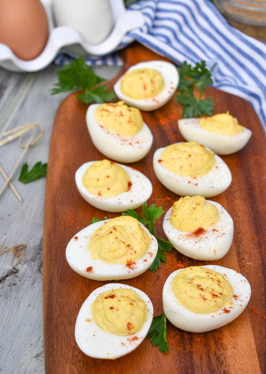classic deviled eggs arranged on a wooden cutting board with fresh herbs and toothpicks on the side