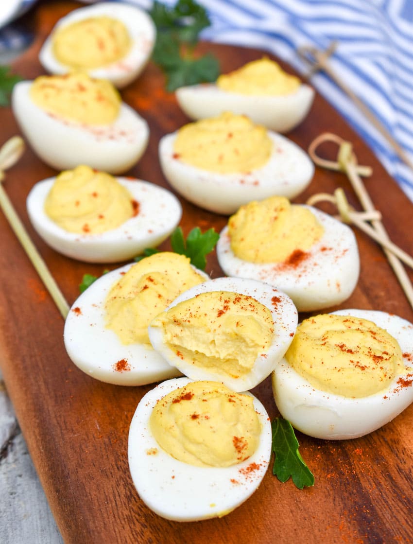 classic deviled eggs arranged on a wooden cutting board with fresh herbs and toothpicks on the side
