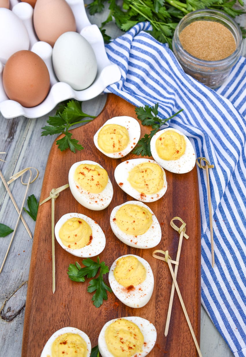 classic deviled eggs arranged on a wooden cutting board with fresh herbs and toothpicks on the side