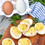 classic deviled eggs arranged on a wooden cutting board with fresh herbs and toothpicks on the side