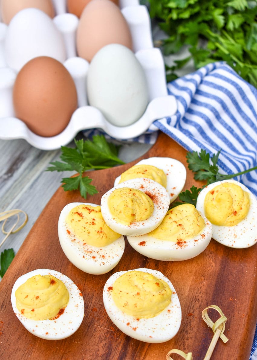 classic deviled eggs arranged on a wooden cutting board with fresh herbs and toothpicks on the side
