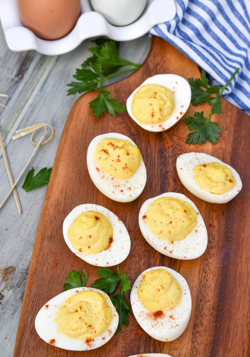 classic deviled eggs arranged on a wooden cutting board with fresh herbs and toothpicks on the side