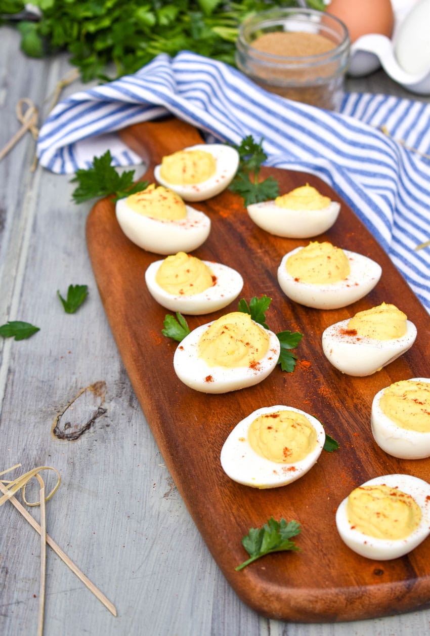 classic deviled eggs arranged on a wooden cutting board with fresh herbs and toothpicks on the side