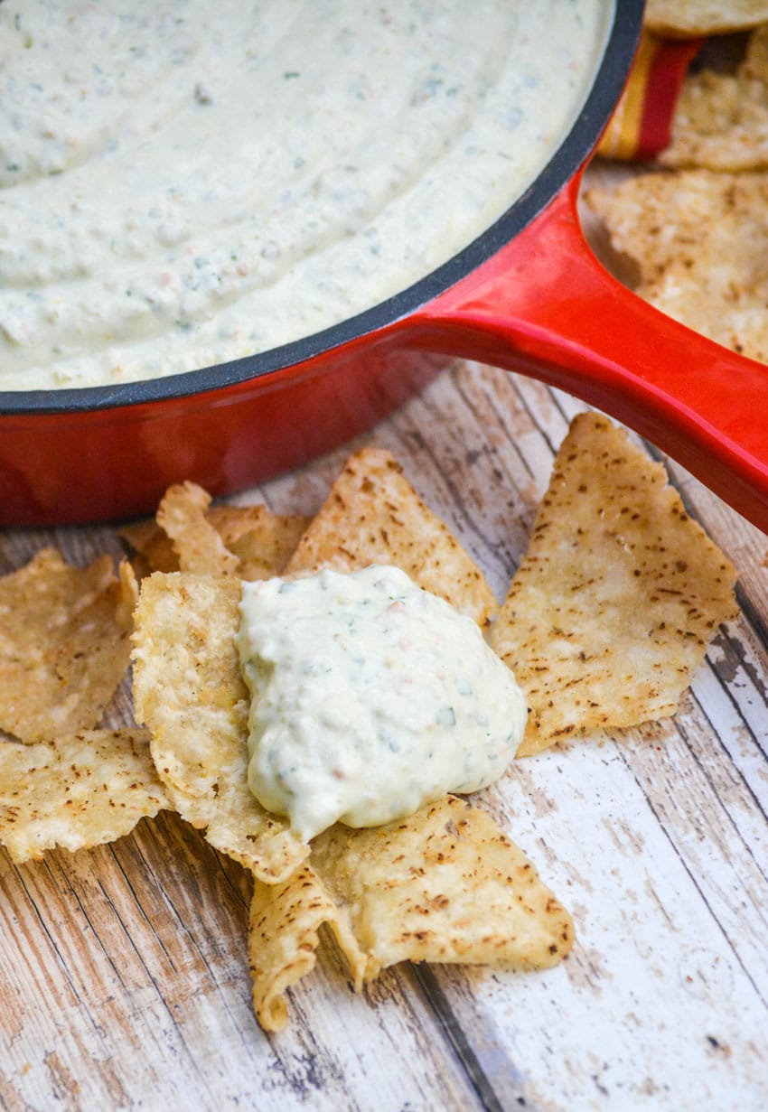 creamy jalapeno dip on a yellow corn tortilla chip sitting on a wooden table