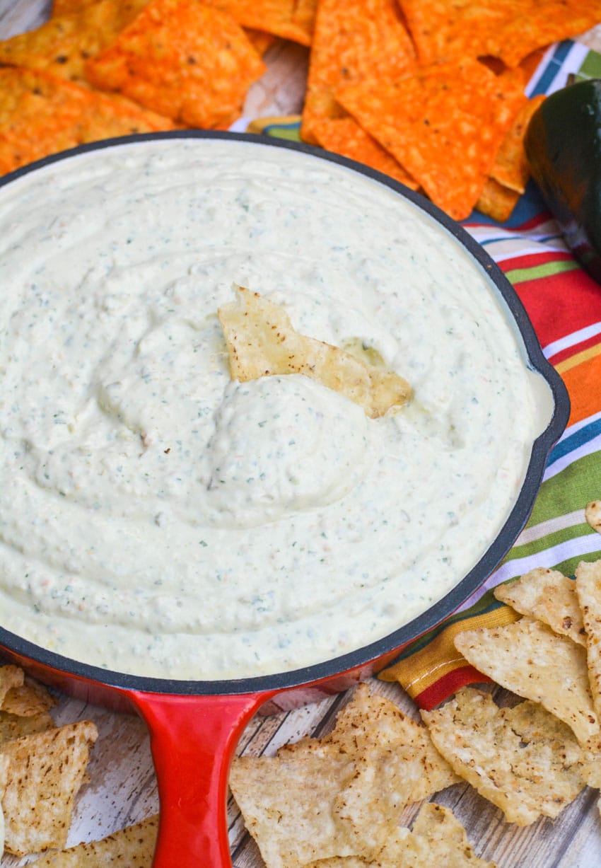 a red skillet filled with creamy jalapeno dip with a corn tortilla stuck in the center