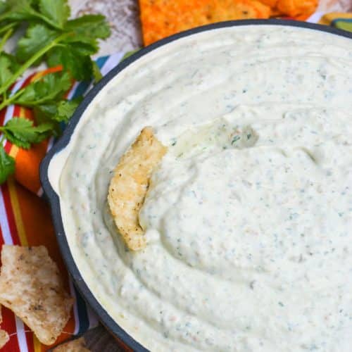 a red skillet filled with creamy jalapeno dip with a corn tortilla stuck in the center