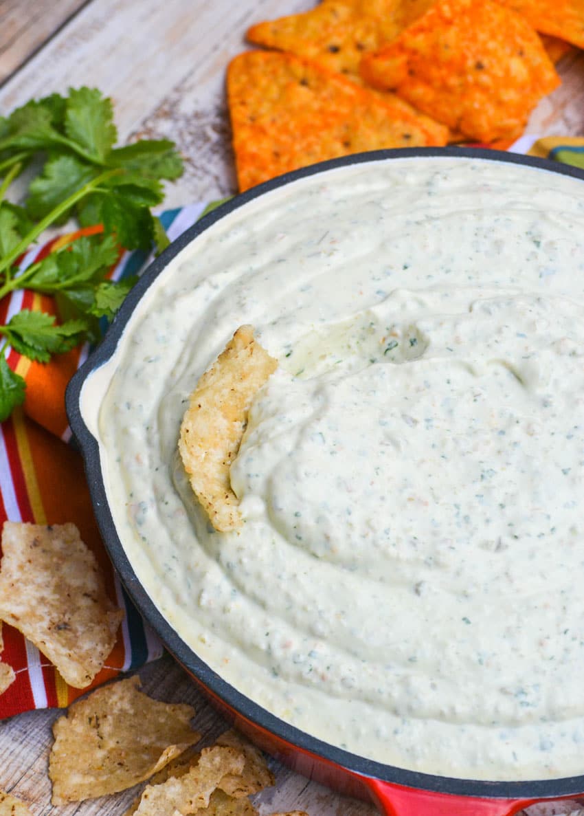 a red skillet filled with creamy jalapeno dip with a corn tortilla stuck in the center