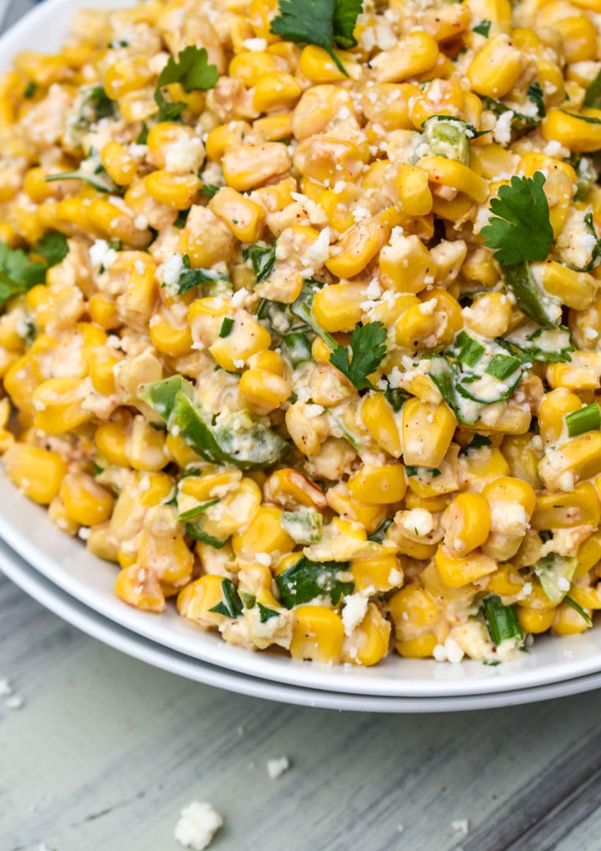 mexican street corn salad in a white bowl topped with crumbled cotija cheese and fresh cilantro leaves