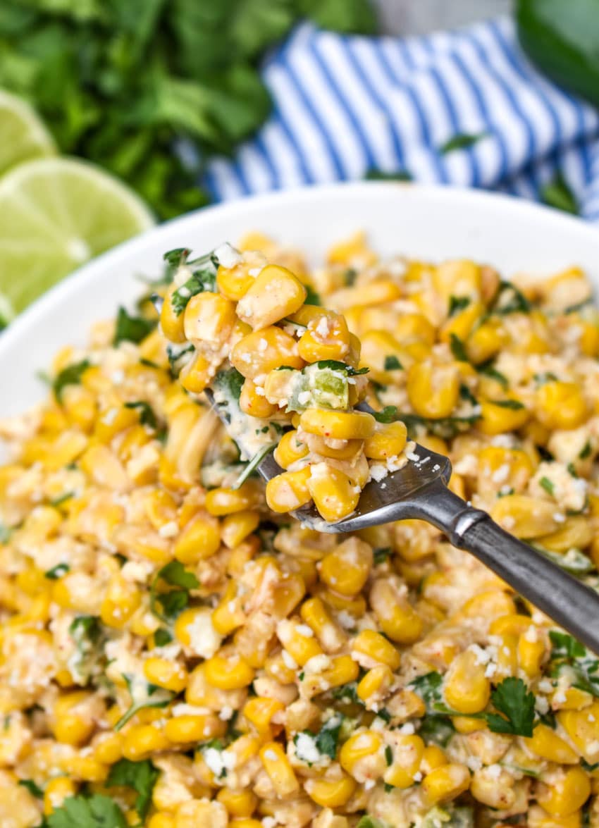 a fork digging into a white bowl filled with esquites street corn salad