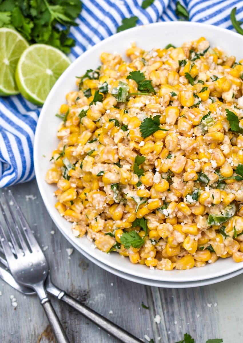 mexican street corn salad in a white bowl topped with crumbled cotija cheese and fresh cilantro leaves