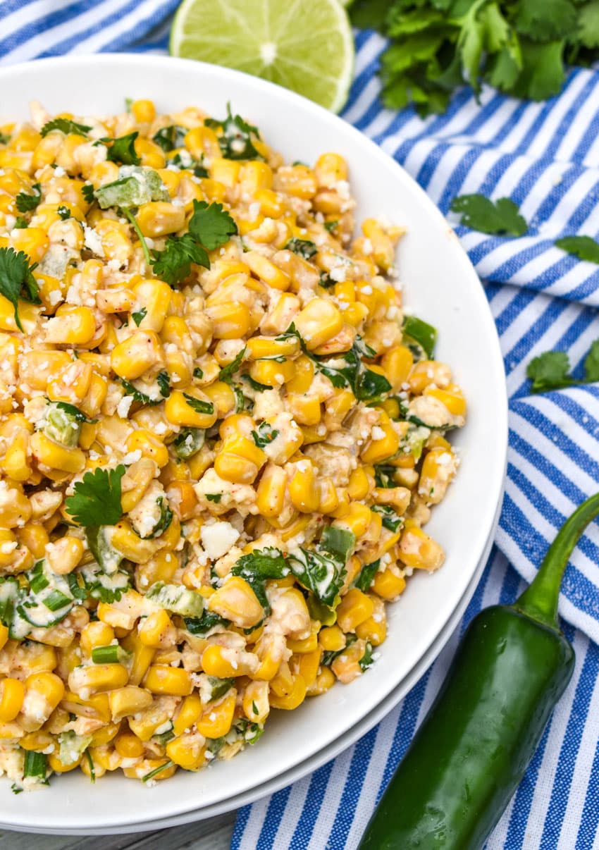 mexican street corn salad in a white bowl topped with crumbled cotija cheese and fresh cilantro leaves