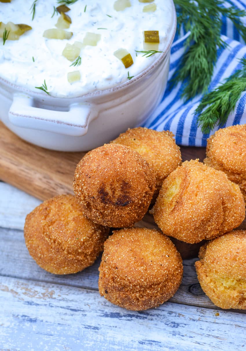 easy homemade hushpuppies in a pile in front of a gray bowl filled with dill pickle dip
