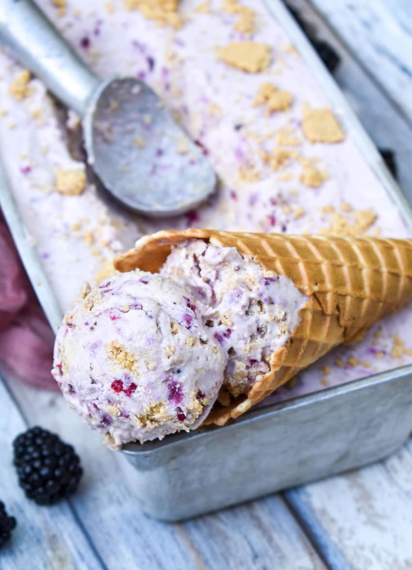 scoops of blackberry cheesecake ice cream in a waffle cone resting in a metal loaf pan