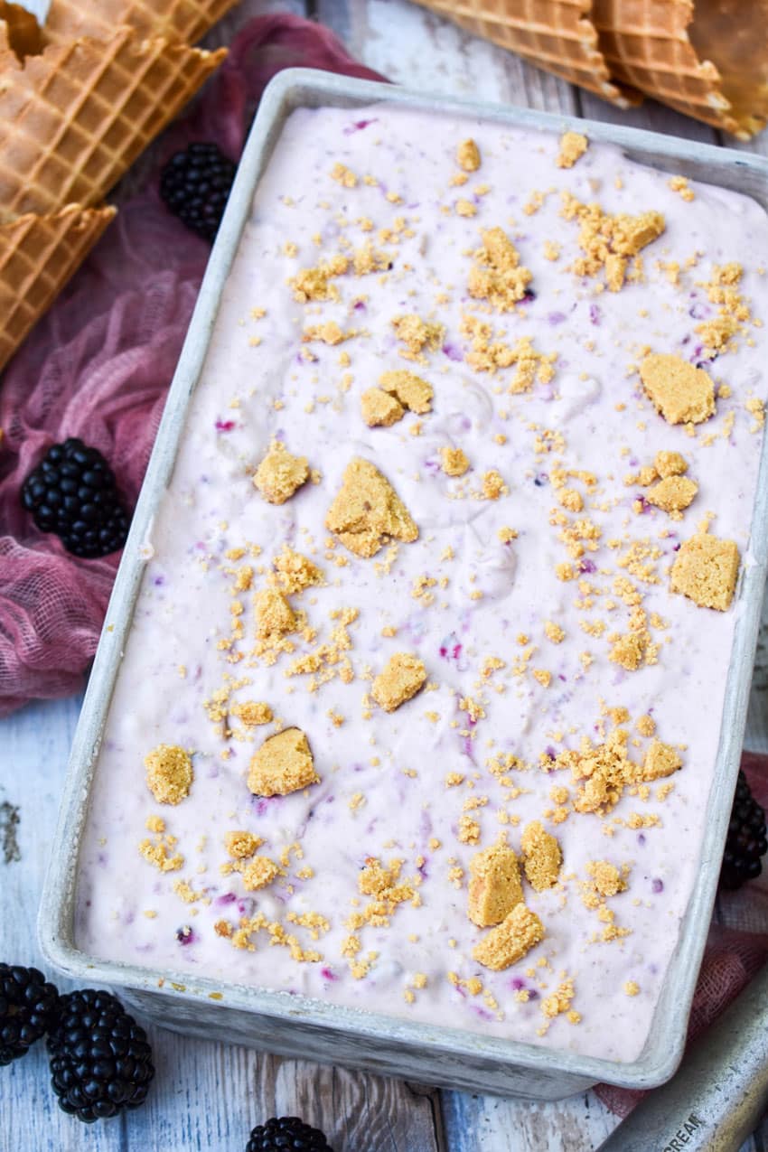 no churn blackberry cheesecake ice cream in a metal loaf pan topped with graham cracker pieces