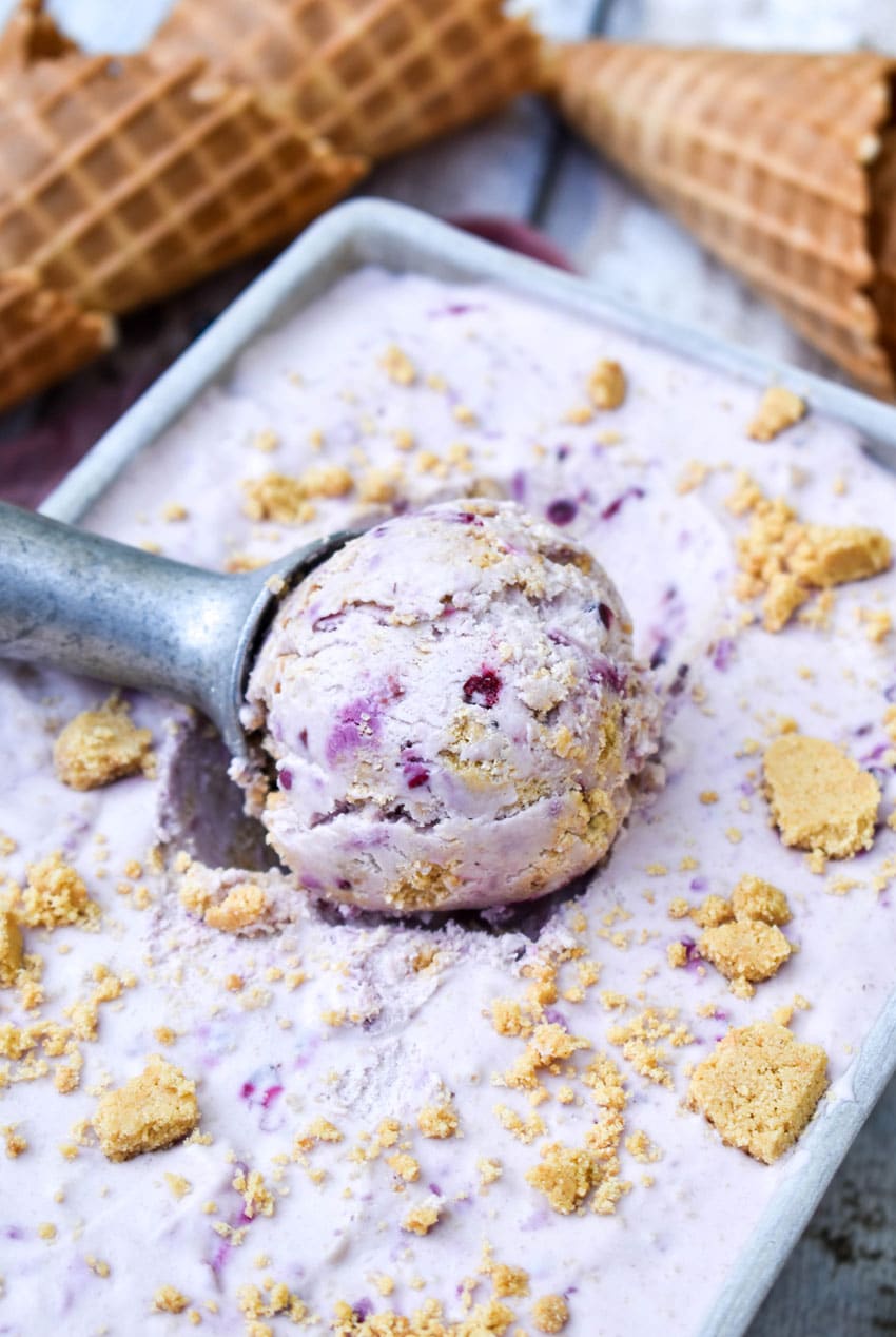 a silver ice cream scooper scooping no churn blackberry cheesecake ice cream out of a metal loaf pan