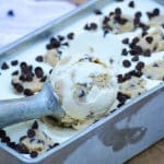 a silver ice cream scoop with a ball of no churn cookie dough ice cream in a metal loaf pan