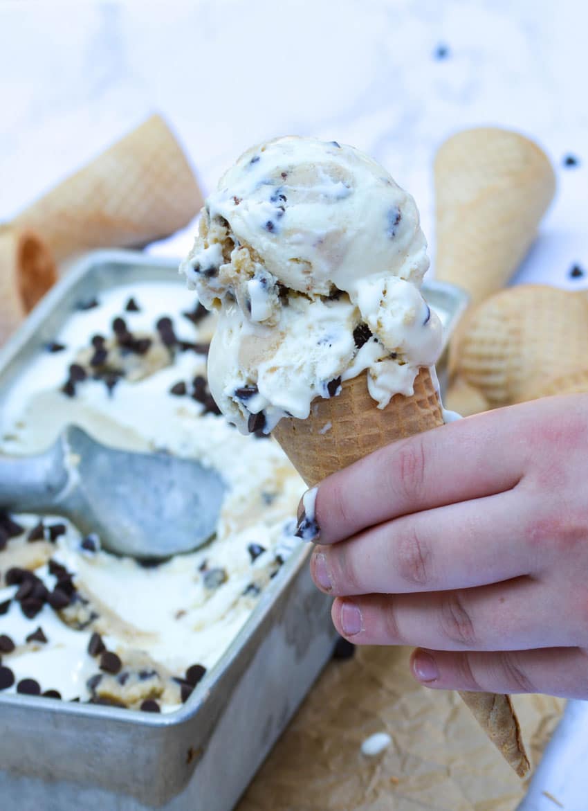 a hand holding a sugar cone topped with two scoops of no churn cookie dough ice cream