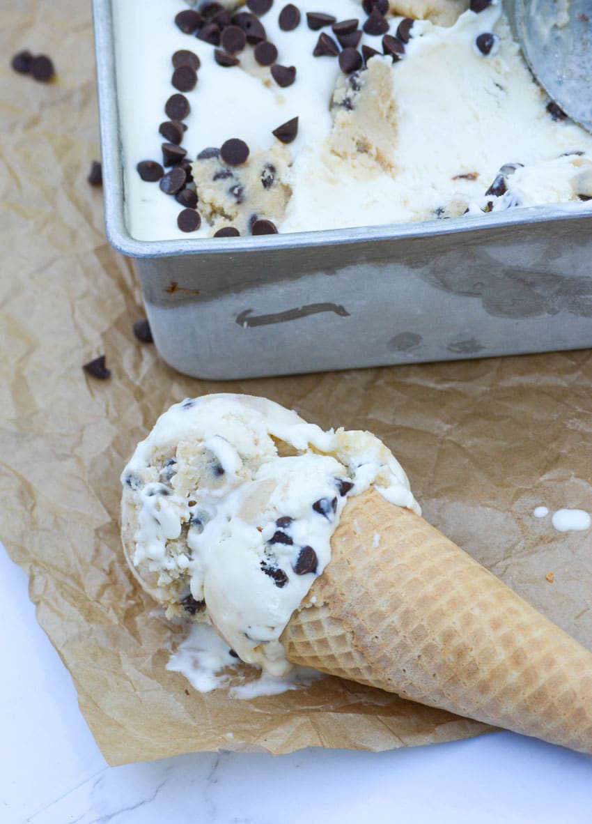 a chocolate chip cookie dough ice cream cone laying on a sheet of brown parchment paper