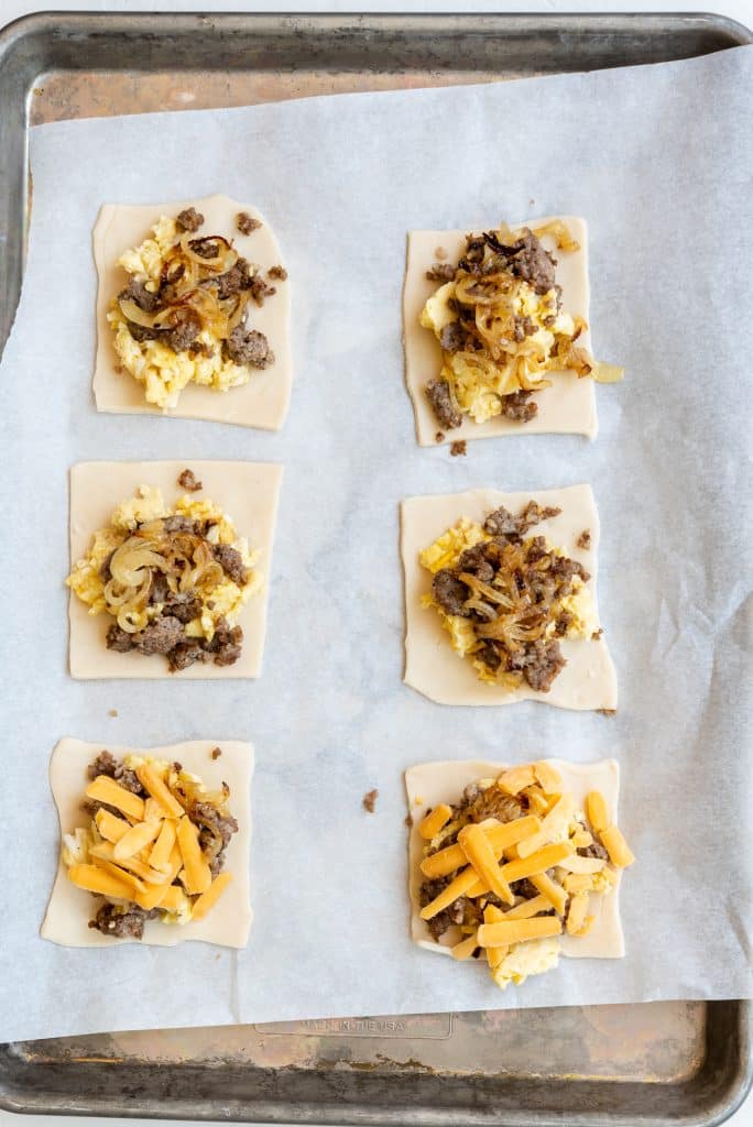 unbaked pastry squares topped with sauce and cheese on a parchment lined baking sheet