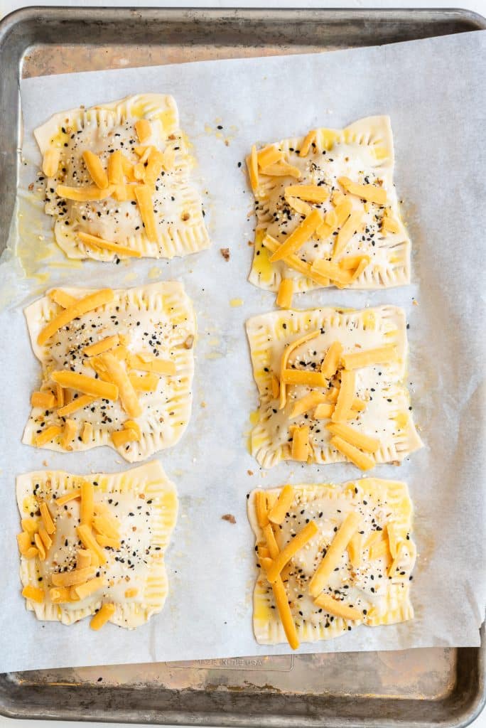 unbaked pastry squares topped with sauce and cheese on a parchment lined baking sheet