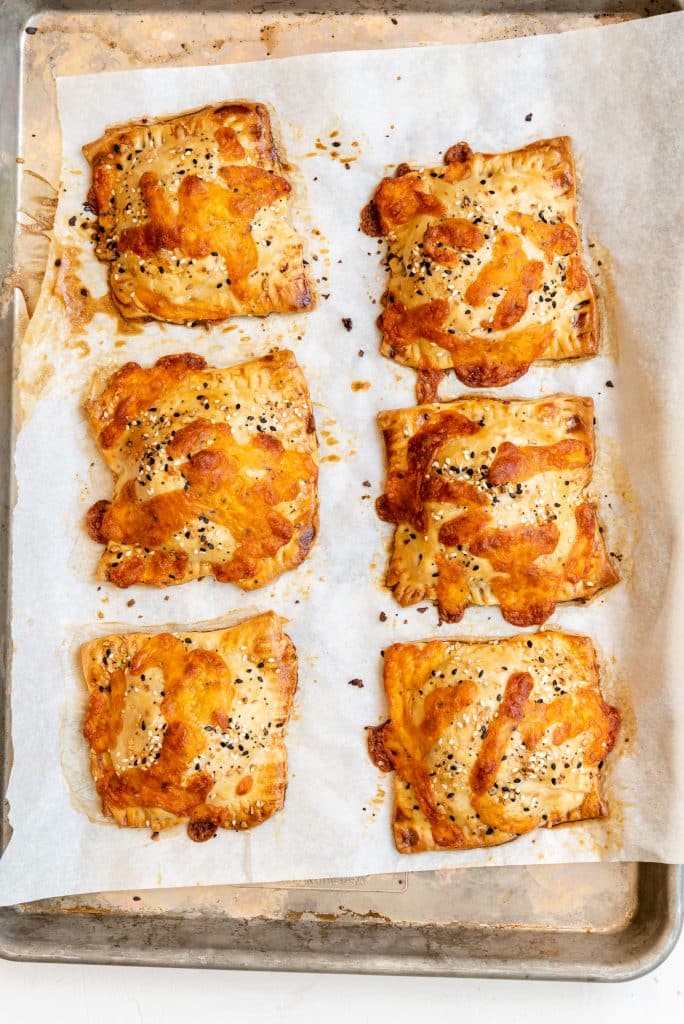 cheesy baked breakfast hand pies on a parchment lined baking sheet
