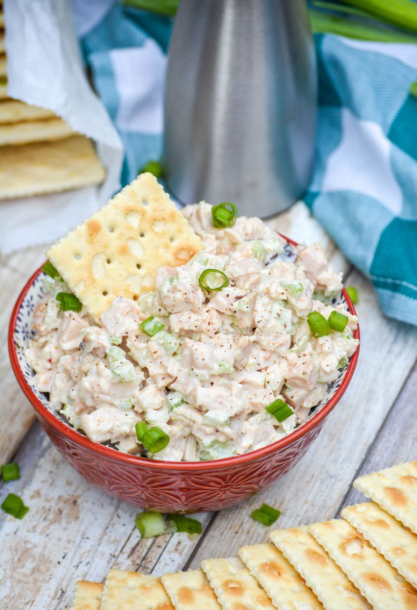 simple Southern chicken salad in a red bowl topped with sliced green onions and a saltine cracker