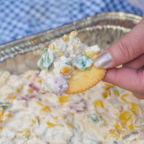 a hand holding up a ritz cracker topped with smoked creamy corn dip