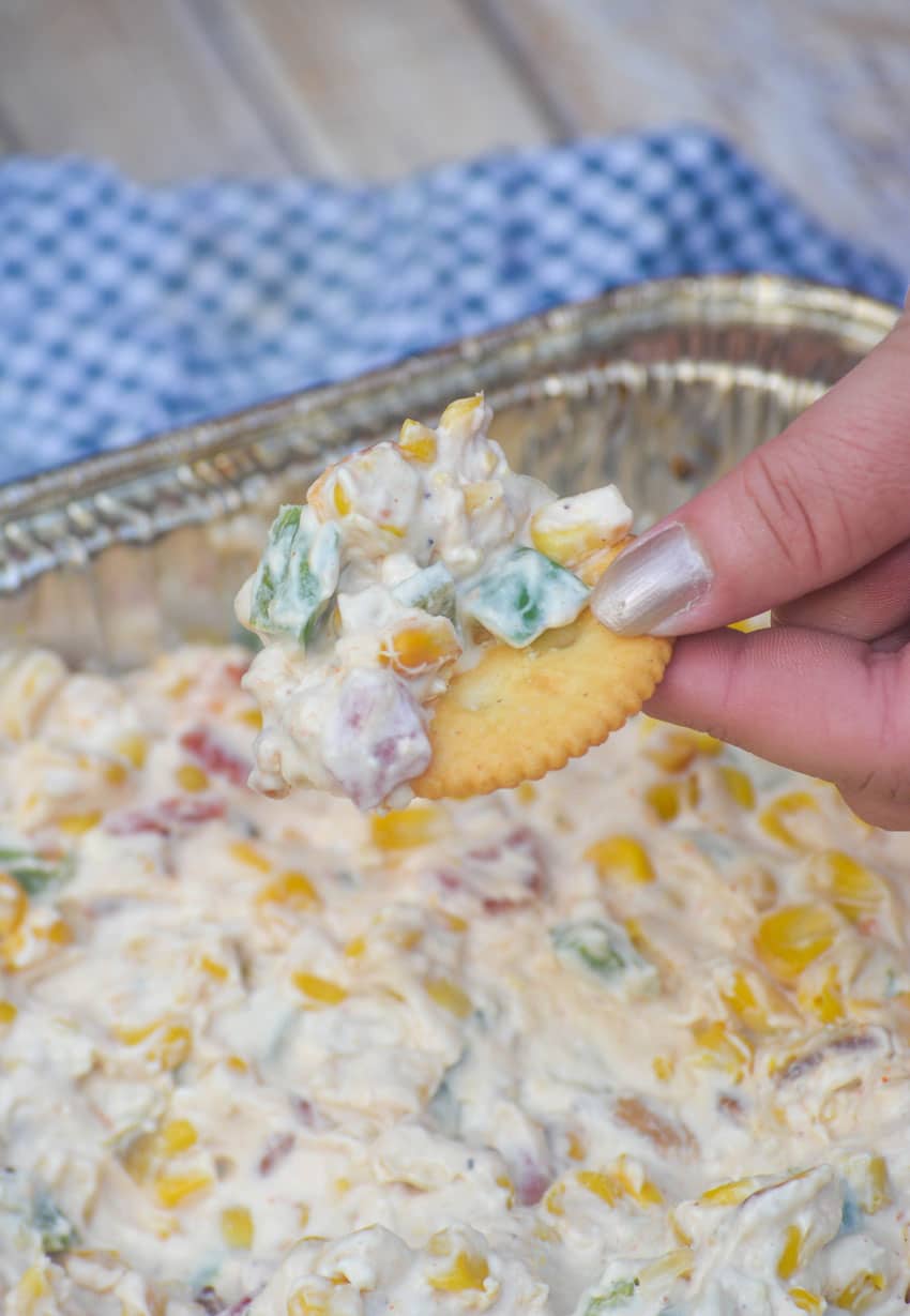 a hand holding up a ritz cracker topped with smoked creamy corn dip