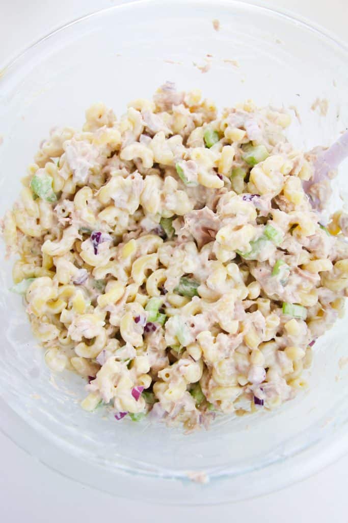 creamy tuna noodle pasta salad with celery and red onion in a glass mixing bowl
