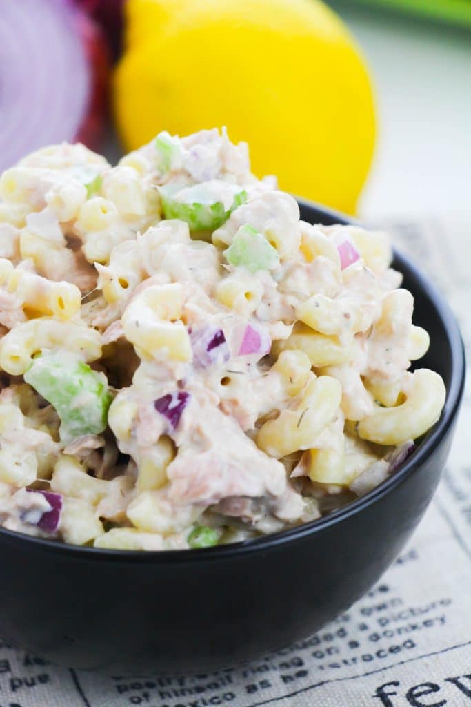 tuna macaroni salad in a black bowl with a lemon and red onion in the background