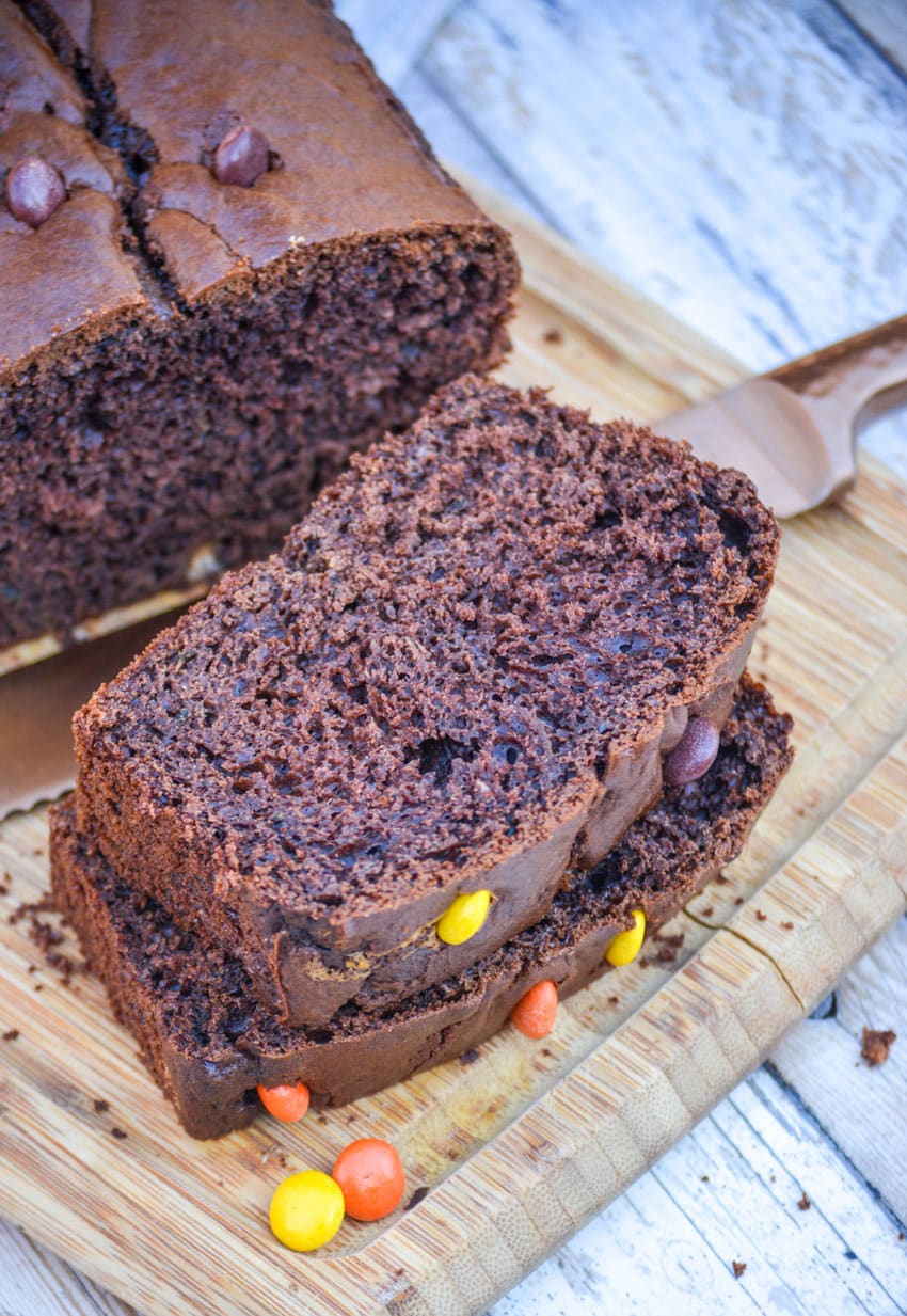 three sliced of chocolate zucchini bread stacked together on a wooden cutting board