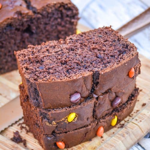 three sliced of chocolate zucchini bread stacked together on a wooden cutting board