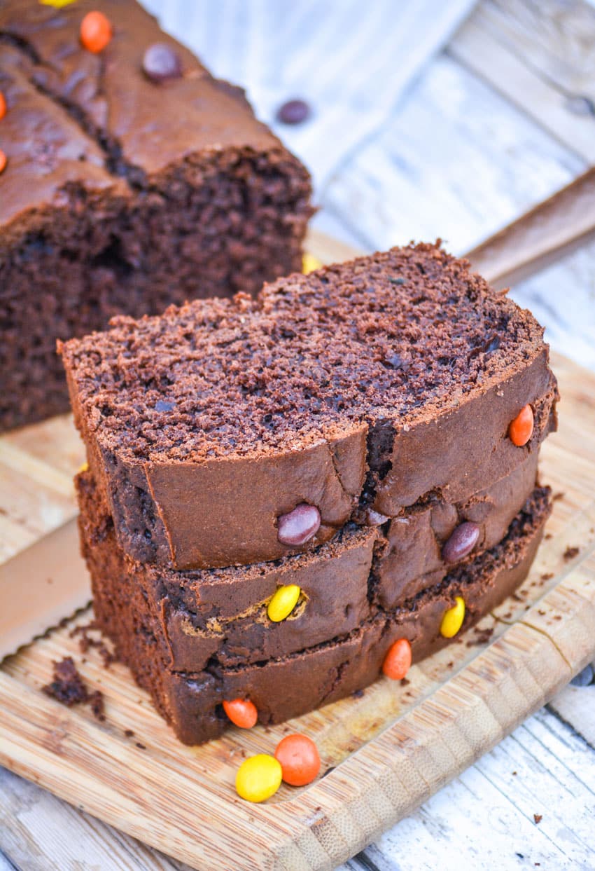 three sliced of chocolate zucchini bread stacked together on a wooden cutting board