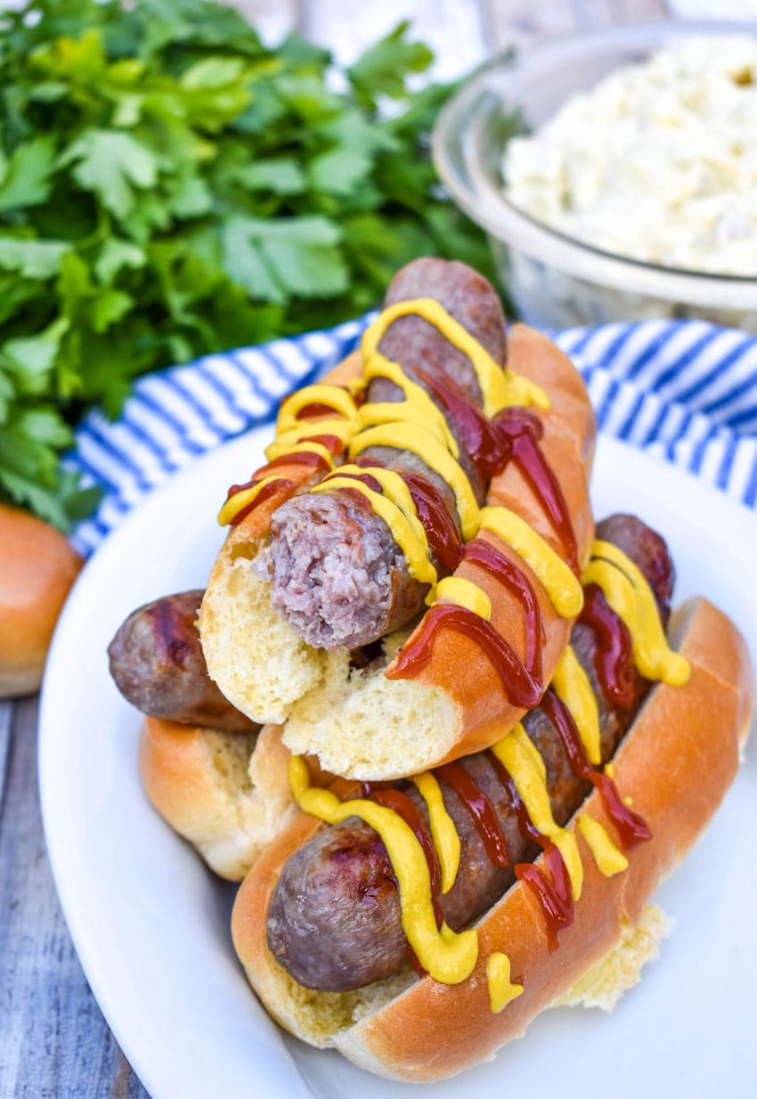 mustard and ketchup drizzled air fryer beer brats stacked on a white serving platter