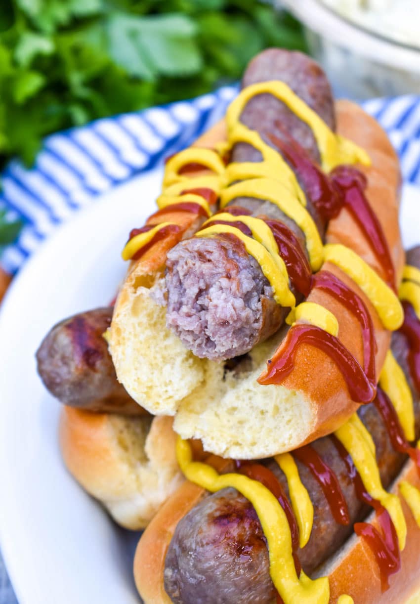 mustard and ketchup drizzled air fryer beer brats stacked on a white serving platter