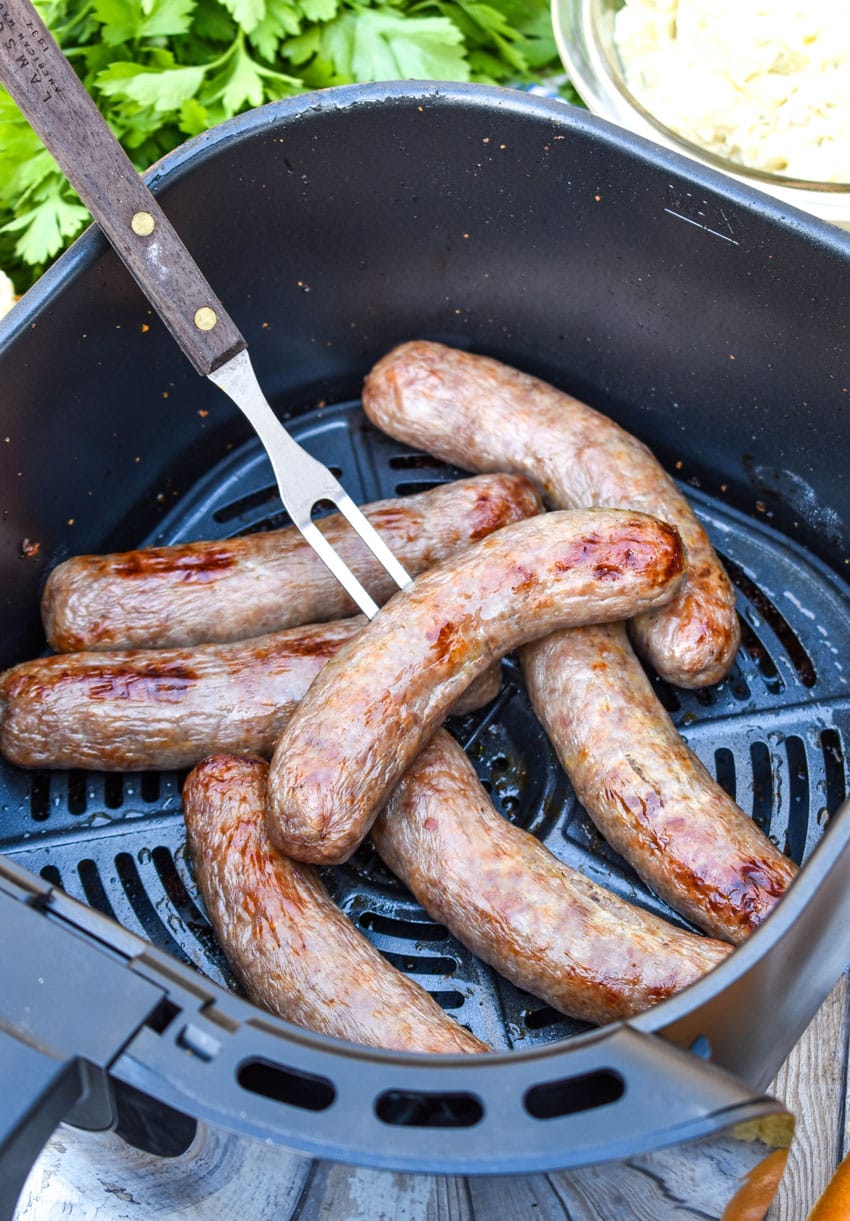 a meat fork stuck in a beer brat in an air fryer basket