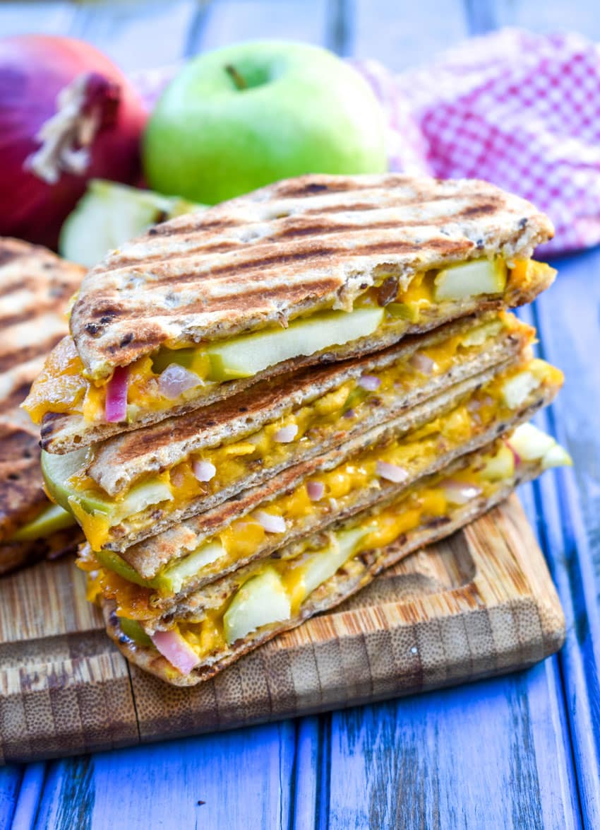 slices of apple cheddar onion paninis stacked on a wooden cutting board