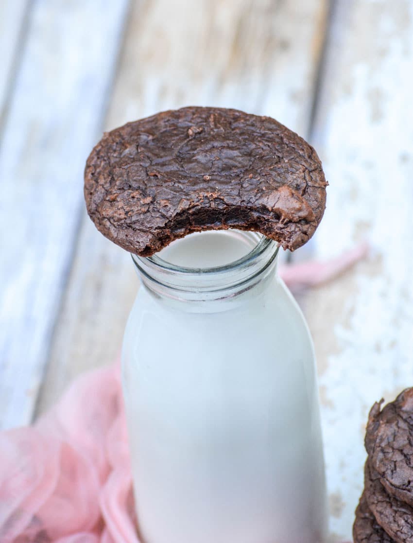 a bitten brownie cookie resting on top of a glass of milk