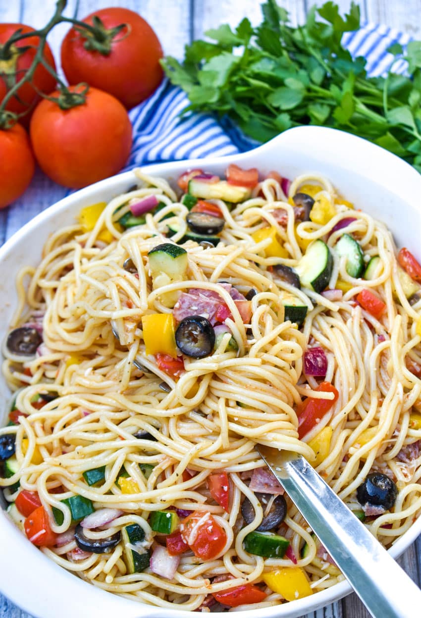 a metal spoon lifting Italian spaghetti salad out of a white mixing bowl