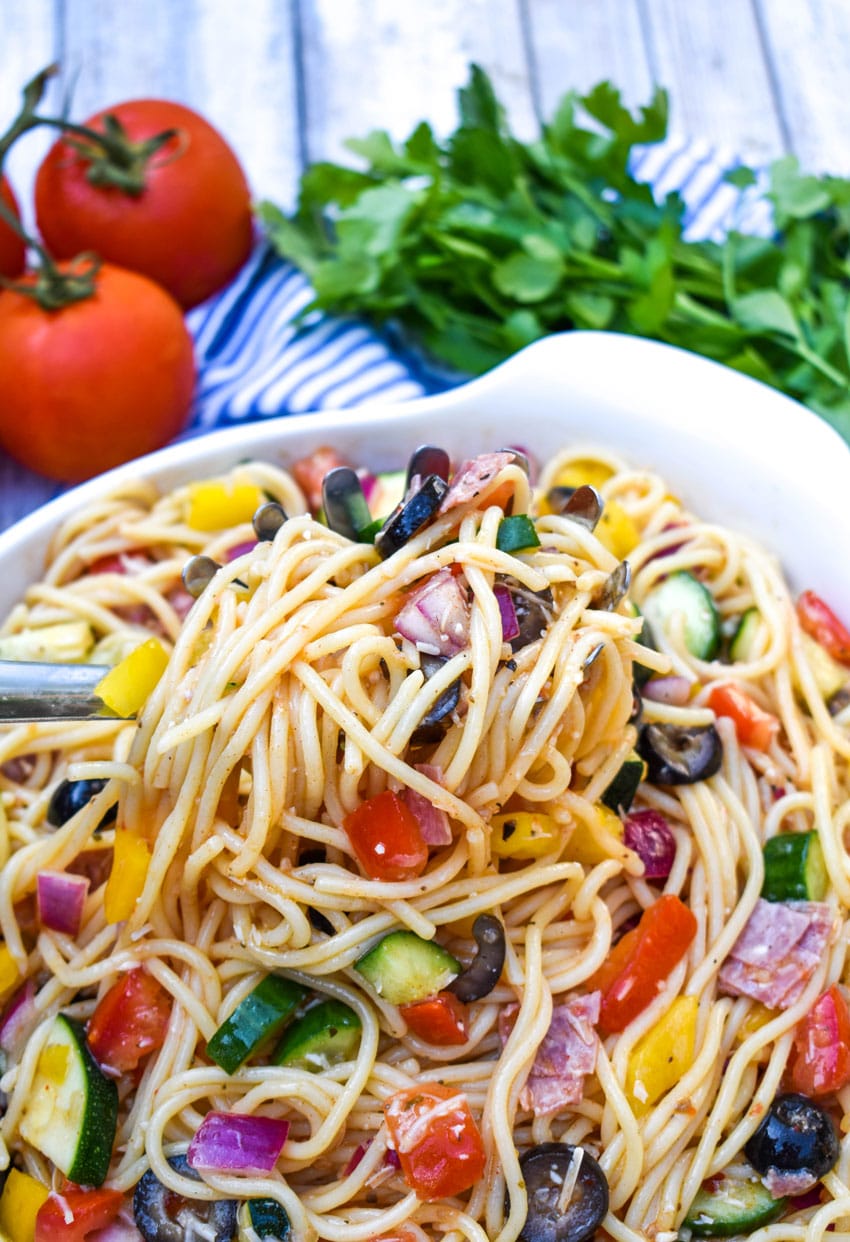 summer spaghetti salad being lifted out of a white bowl by a silver serving spoon