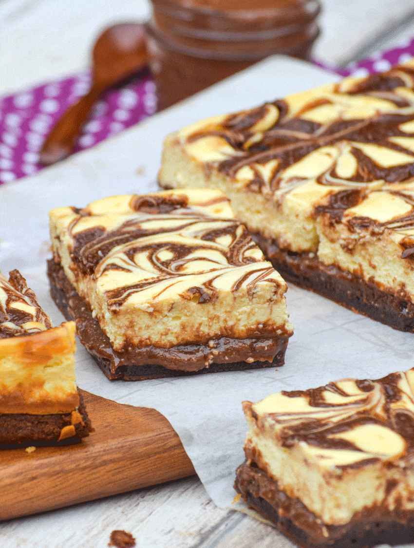 nutella cheesecake brownies cut into squares on a parchment paper covered wooden cutting board