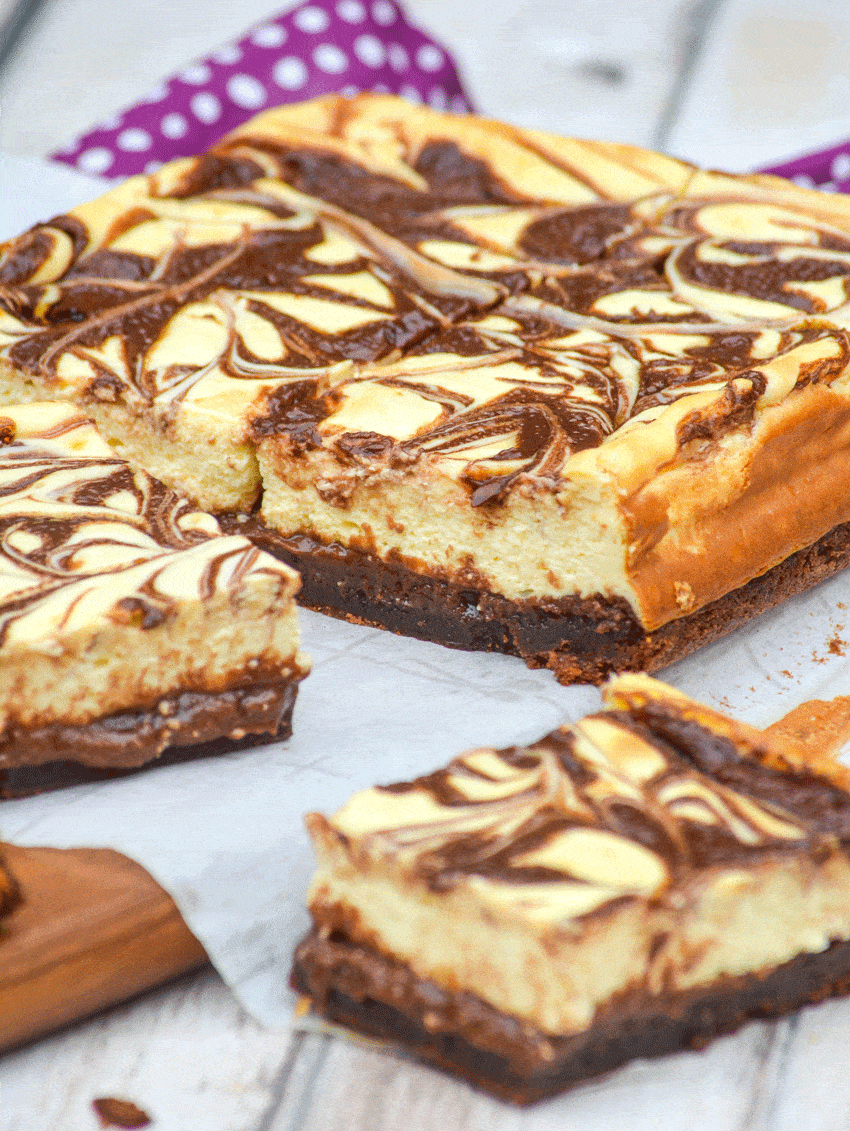 nutella cheesecake brownies cut into squares on a parchment paper covered wooden cutting board