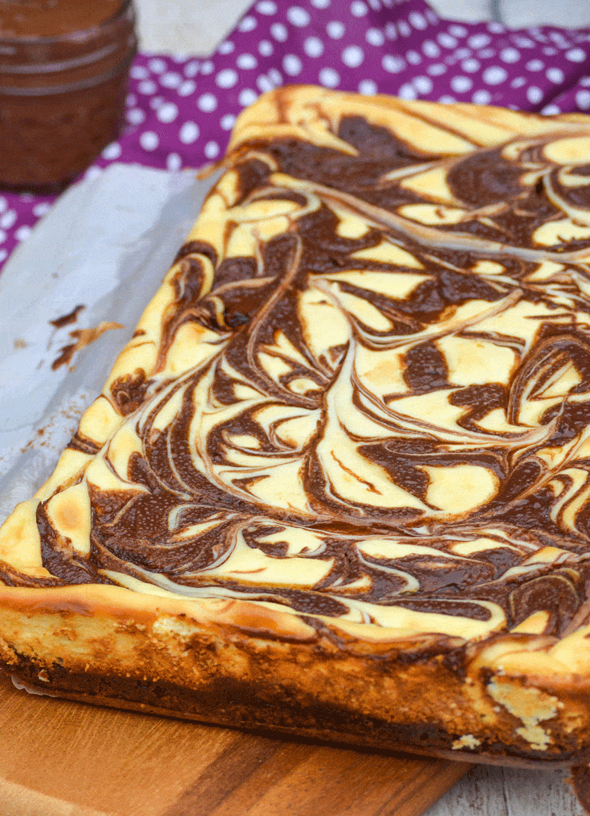 nutella cheesecake brownies on a parchment paper covered wooden cutting board