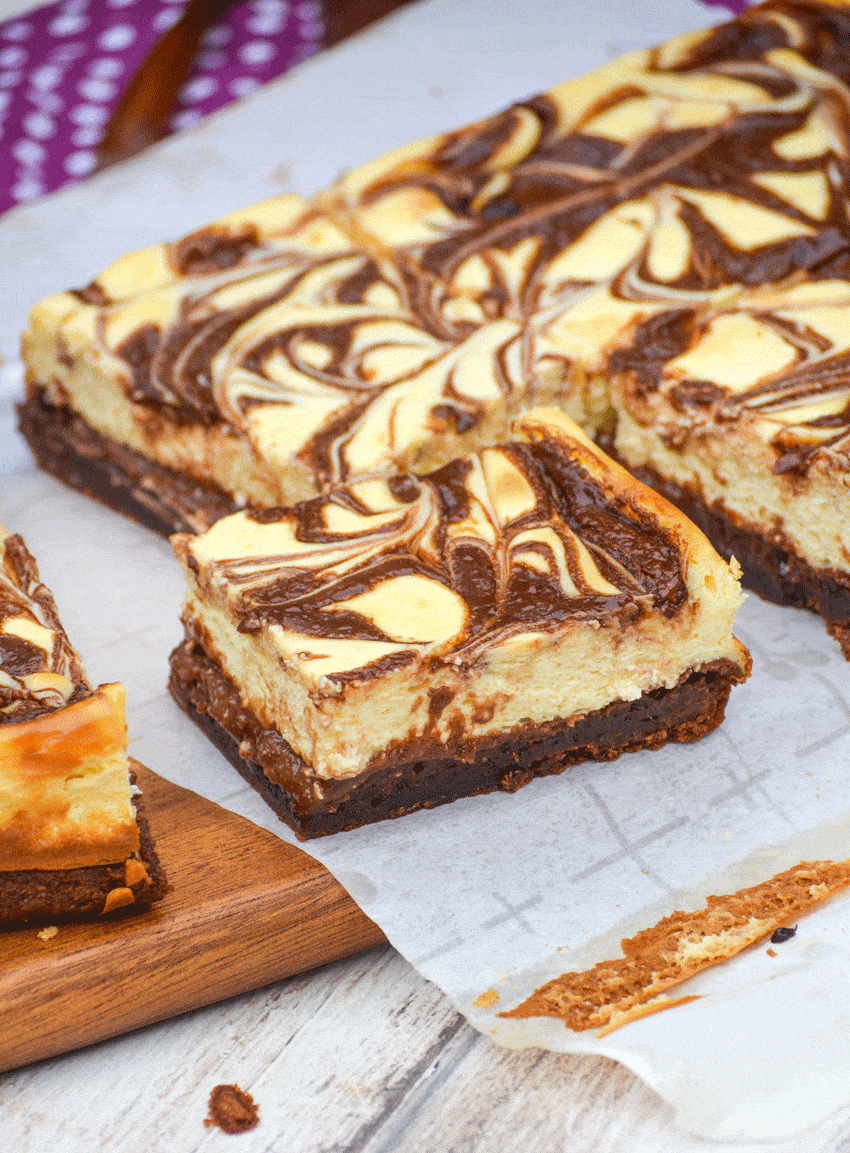 nutella cheesecake brownies cut into squares on a parchment paper covered wooden cutting board