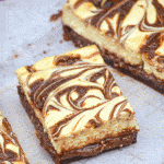 nutella cheesecake brownies cut into squares on a parchment paper covered wooden cutting board
