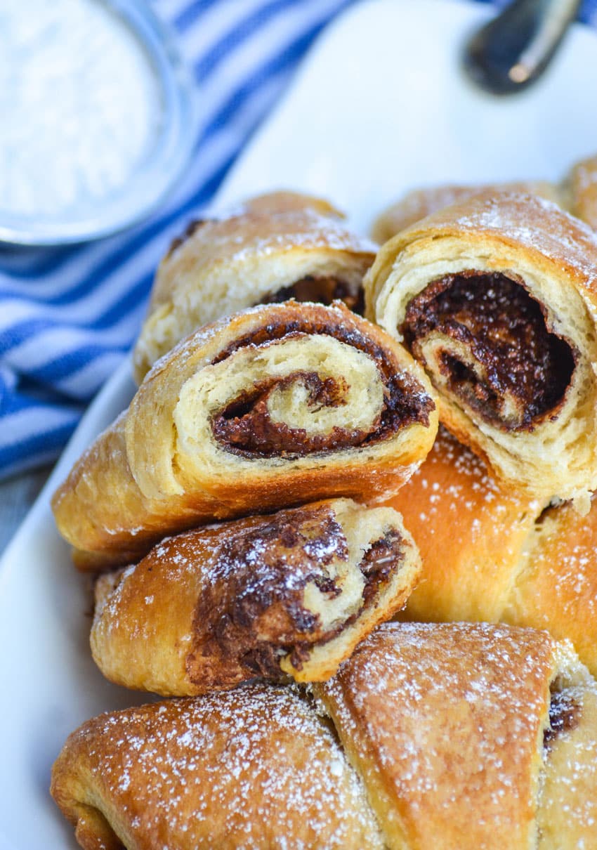 nutella crescent rolls on a white platter torn in half to reveal the nutella swirl inside the rolled pastry