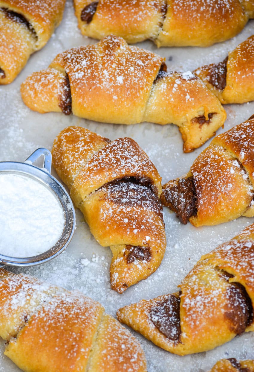 powdered sugar sprinkled nutella crescent rolls on a white parchment paper lined baking sheet