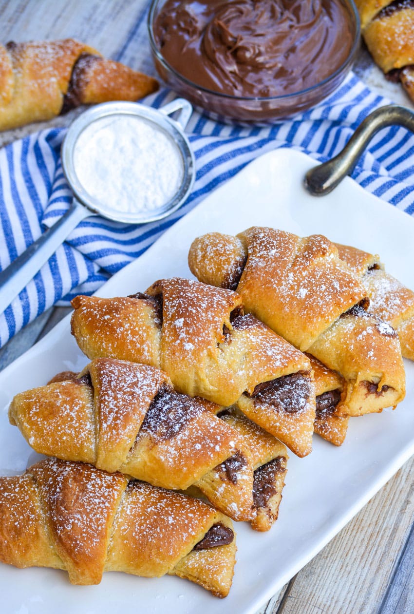 nutella stuffed crescent rolls on a white serving tray sprinkled with powdered sugar
