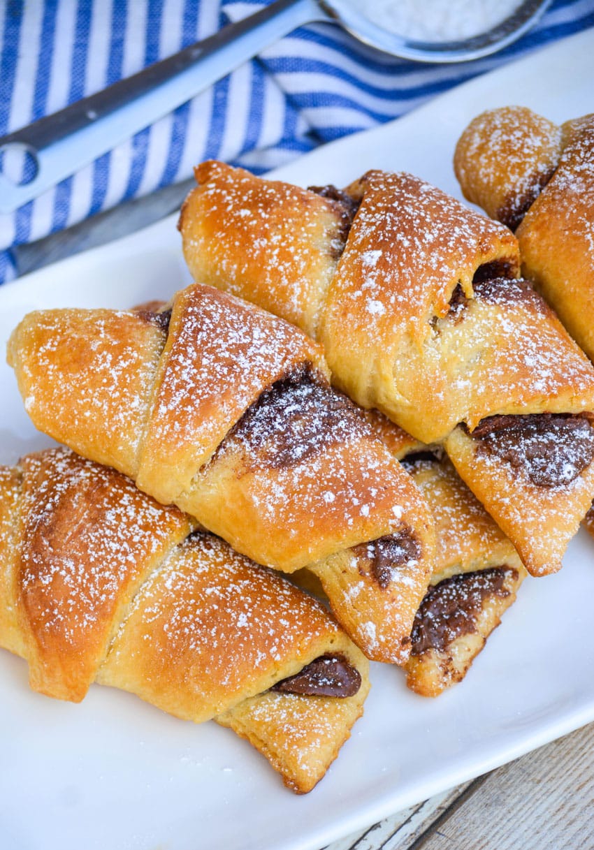nutella stuffed crescent rolls on a white serving tray sprinkled with powdered sugar