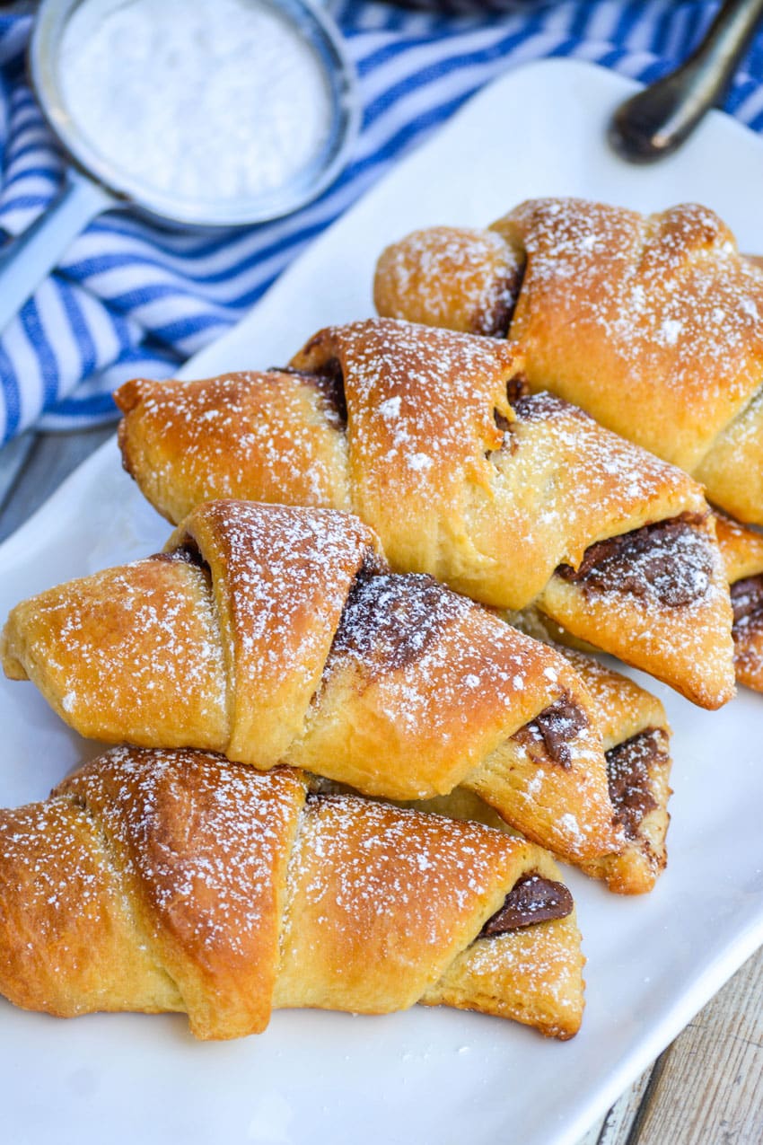 nutella stuffed crescent rolls on a white serving tray sprinkled with powdered sugar